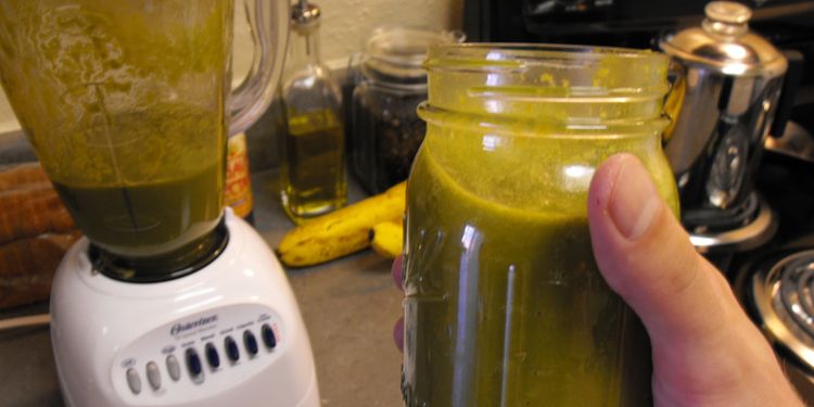 Photo of jar full of stomach aid smoothie held in hand next to a blender